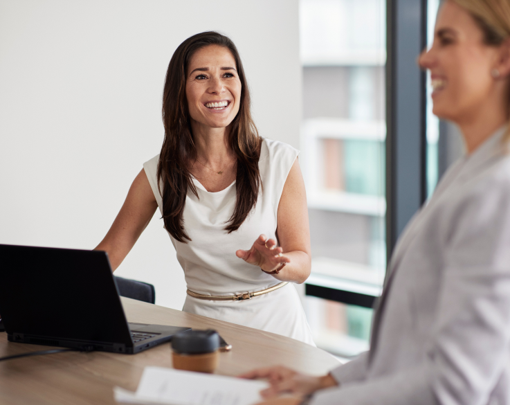 Two standing office employees stand and laugh in front of a laptop